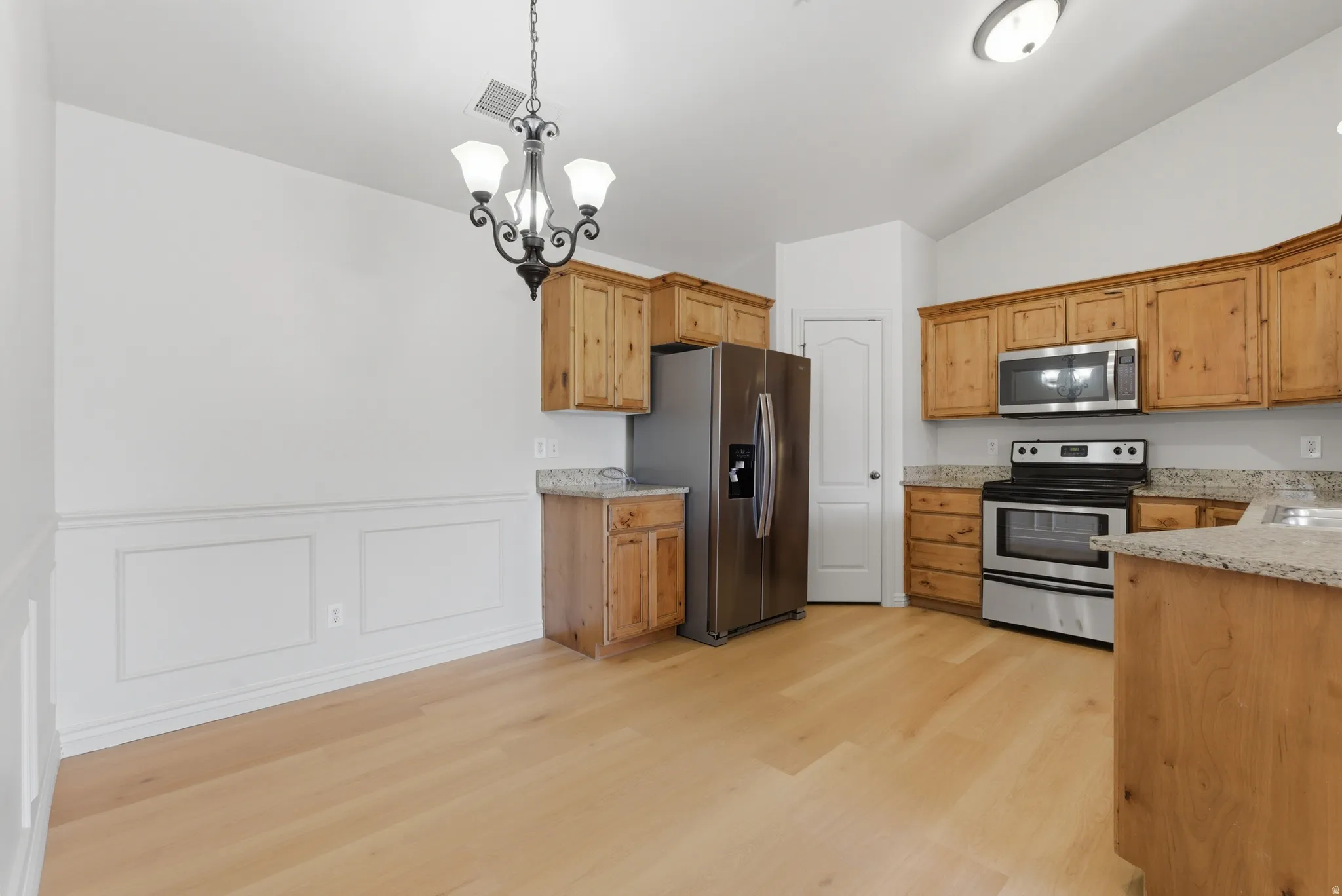 Kitchen featuring stainless steel appliances, a chandelier, light stone countertops, vaulted ceiling, and light wood-style flooring