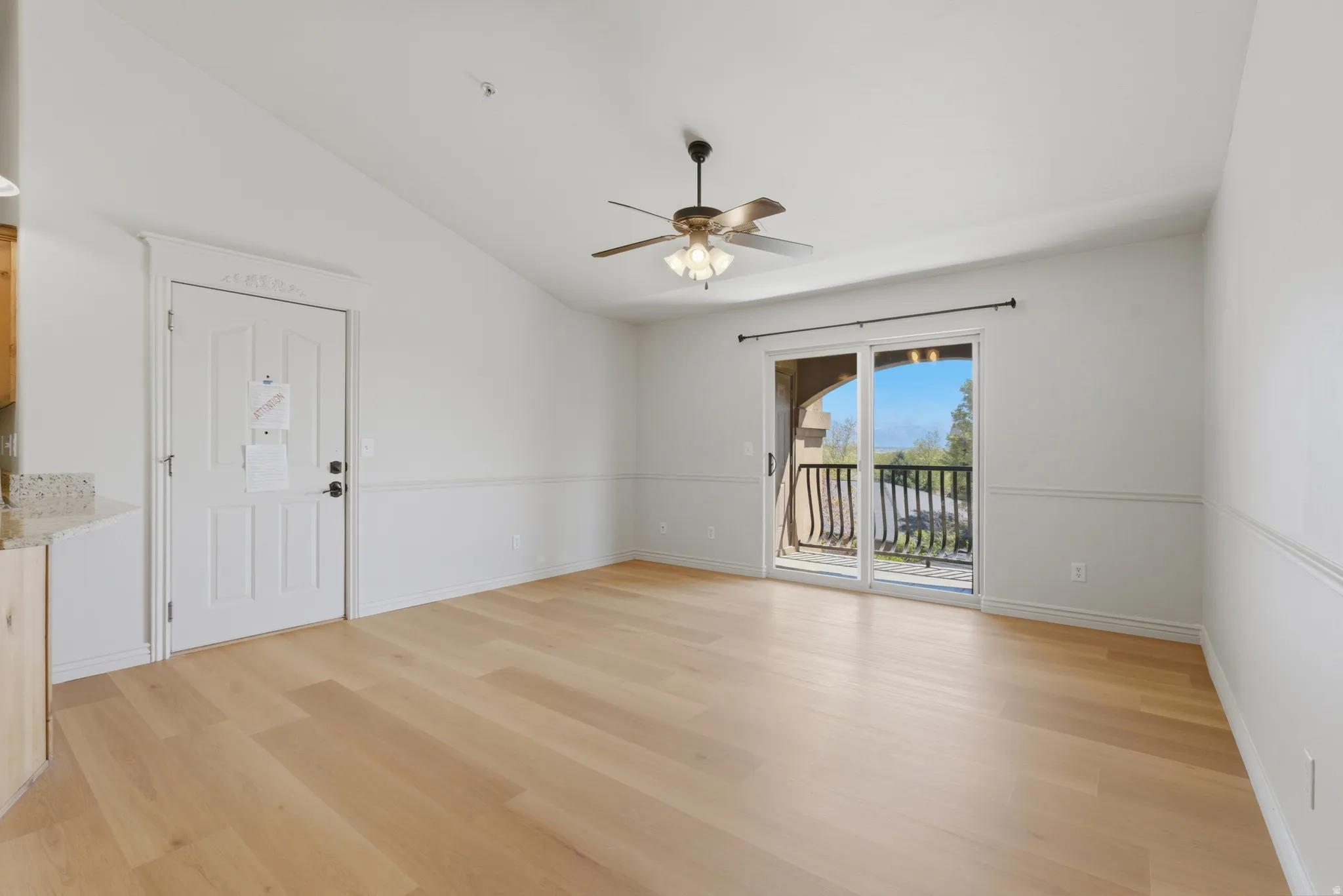 Empty room with vaulted ceiling, ceiling fan, and light wood-style floors
