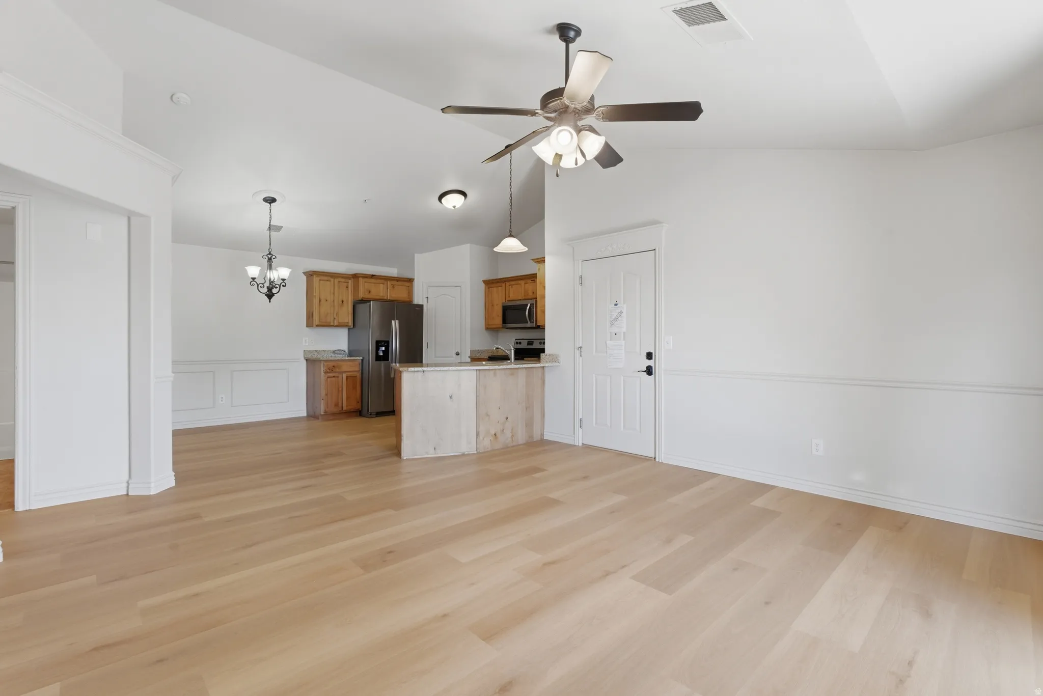 Unfurnished living room featuring suspended lighting, ceiling fan, light wood-style floors, a decorative wall, and wainscoting