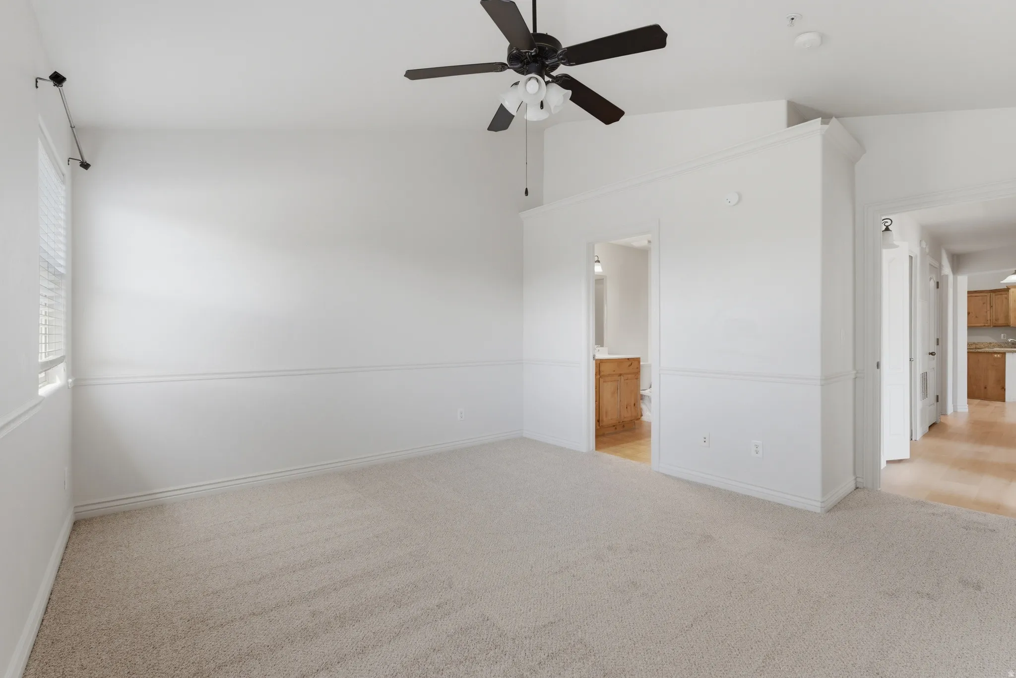 Unfurnished bedroom featuring light carpet, a ceiling fan, vaulted ceiling, and connected bathroom