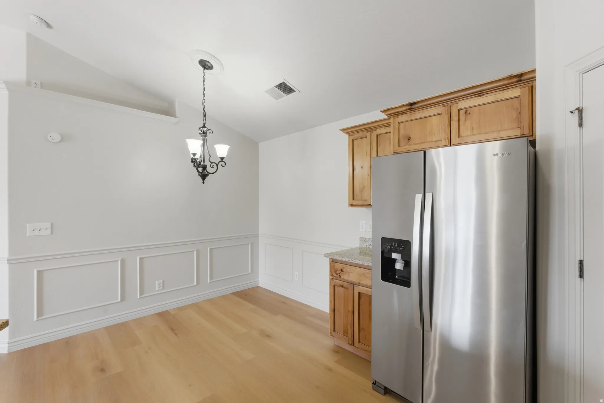 Kitchen with stainless steel refrigerator with ice dispenser, vaulted ceiling, a decorative wall, a wainscoted wall, and light wood-style floors