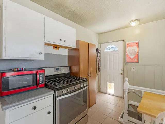 Kitchen featuring stainless steel range with gas cooktop, white cabinets, light countertops, a wainscoted wall, and a textured ceiling.