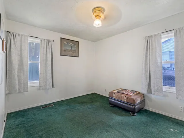 Empty room featuring healthy amount of natural light, dark carpet with hardwood floors underneath.
