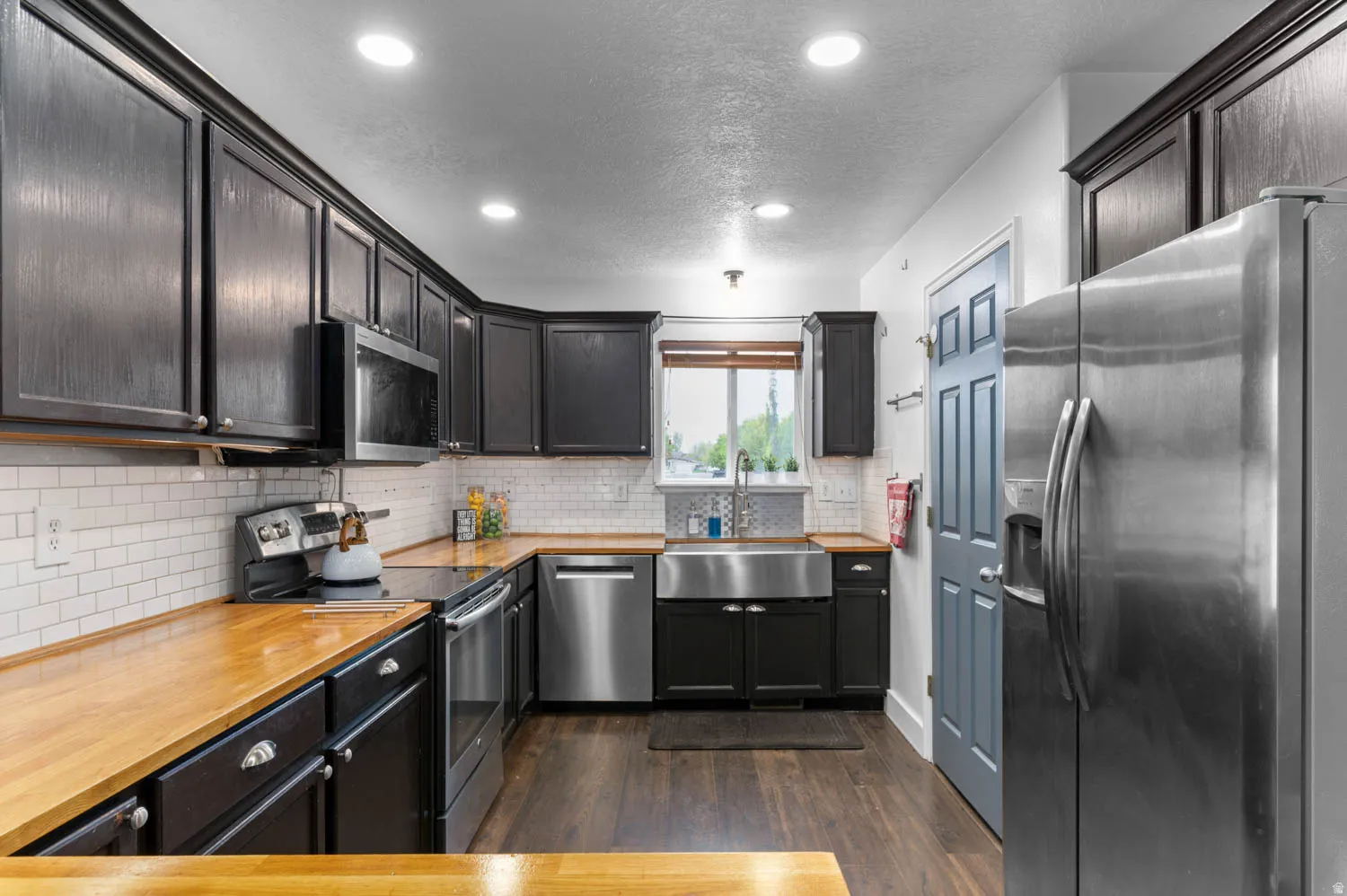 Kitchen with stainless steel appliances, dark wood finished floors, a textured ceiling, recessed lighting, and tasteful backsplash