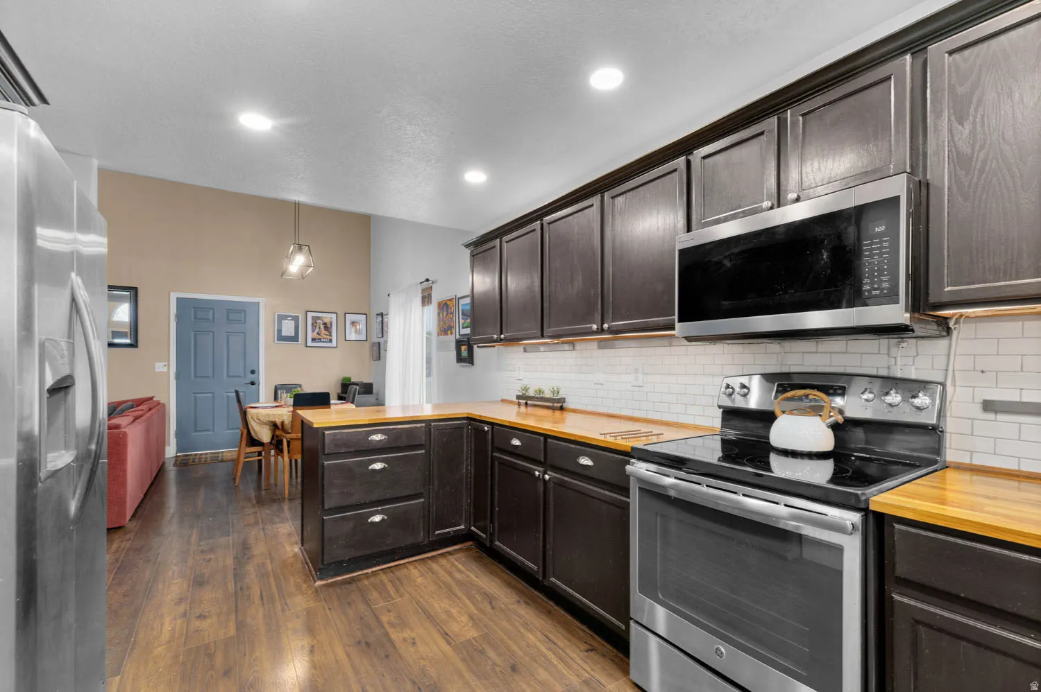 Kitchen featuring stainless steel appliances, butcher block countertops, dark wood finish cabinetry, dark wood-type flooring, and a peninsula
