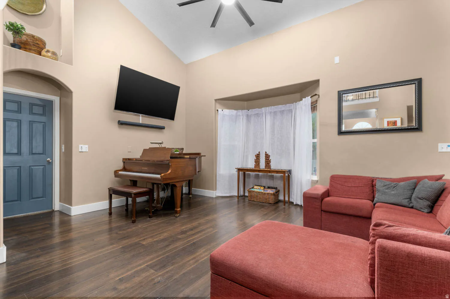 Living area with dark wood-style flooring, lofted ceiling, arched walkways, and ceiling fan