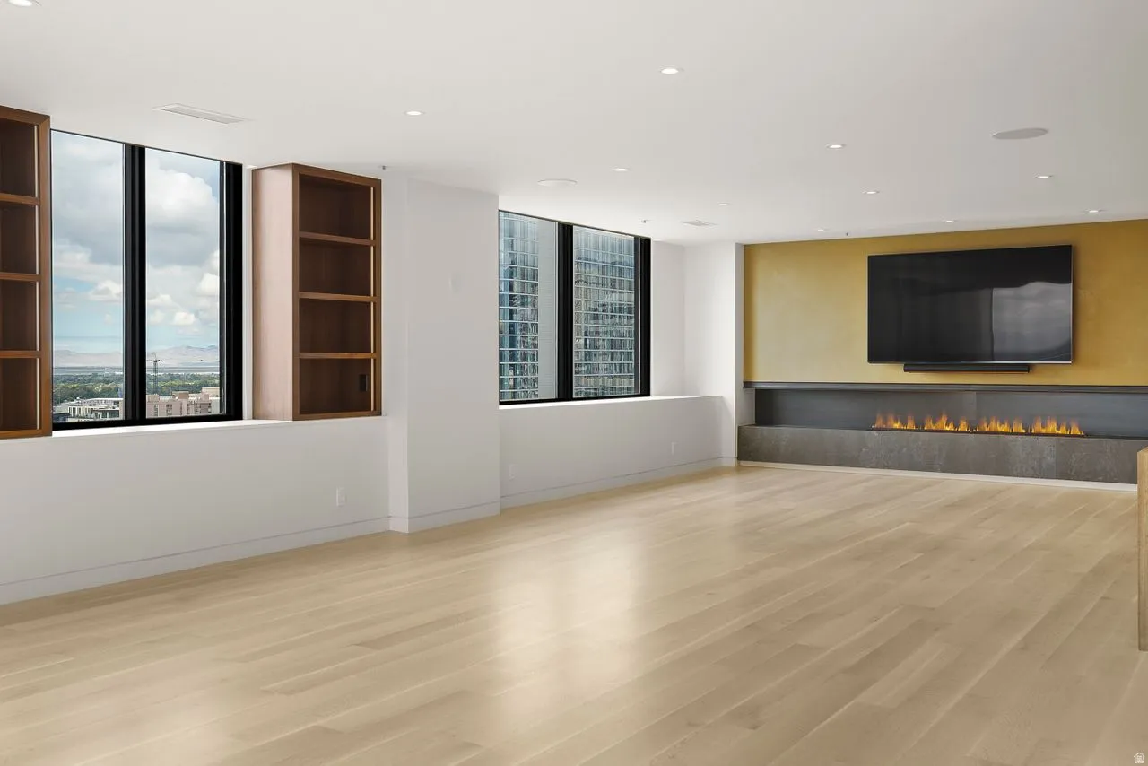 Unfurnished living room with light wood-style floors, recessed lighting, plenty of natural light, and a warm lit fireplace