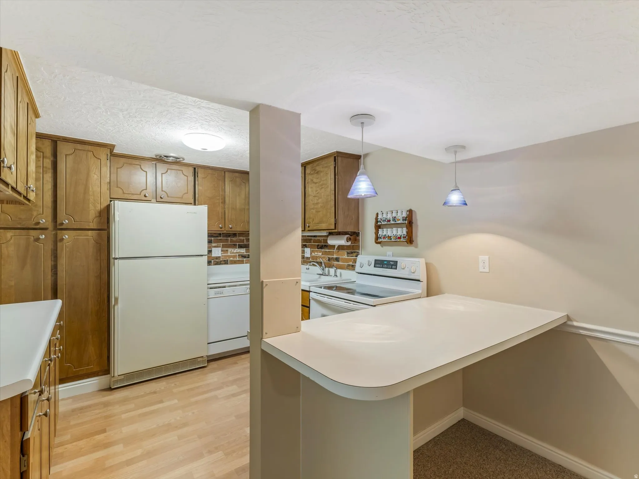Nice efficient kitchen down with a bar and pendant lighting, electric range, dishwasher, and plenty of pantry and prep space