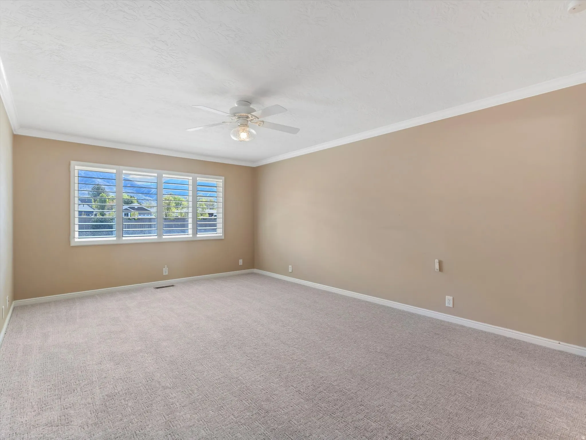 Primary bedroom with new carpet, plantation shutters, mountain views, crown molding, and ceiling fan