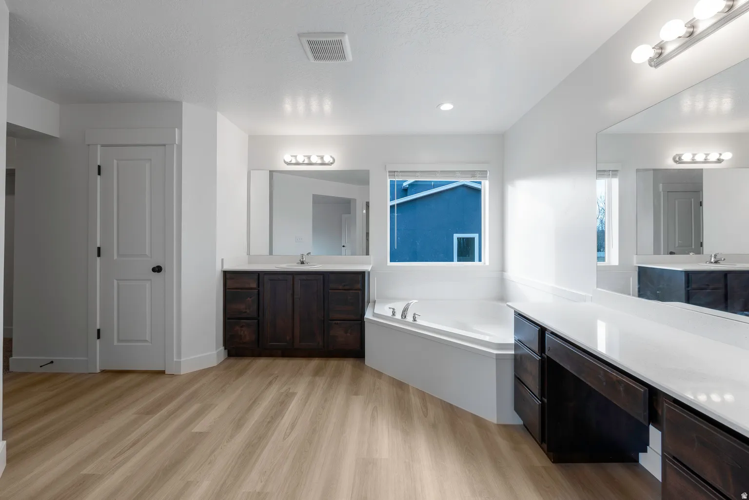 Full bath with two vanities, a garden tub, and light wood-style floors