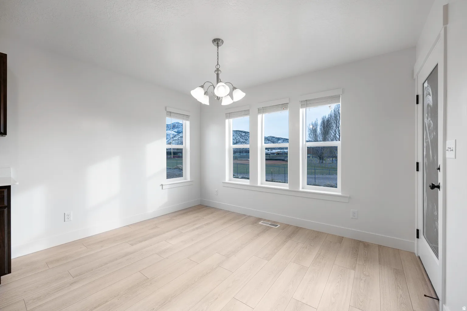 Unfurnished dining area with hanging lights, light wood finished floors, healthy amount of natural light, and a mountain view