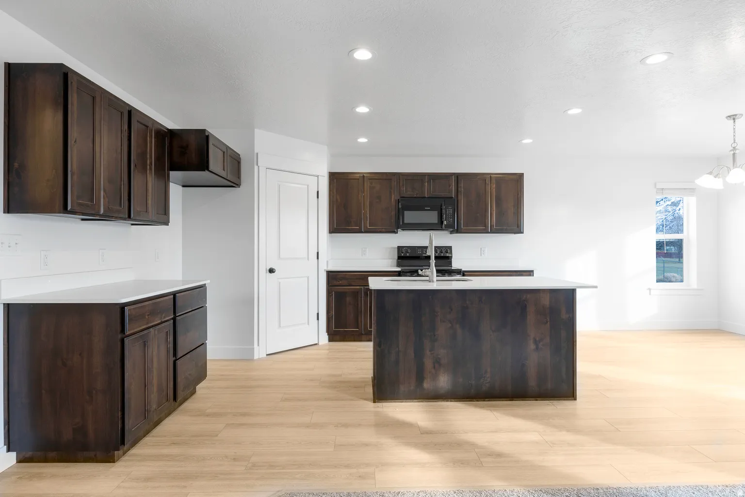 Kitchen with dark wood finish cabinetry, light wood finished floors, and black appliances