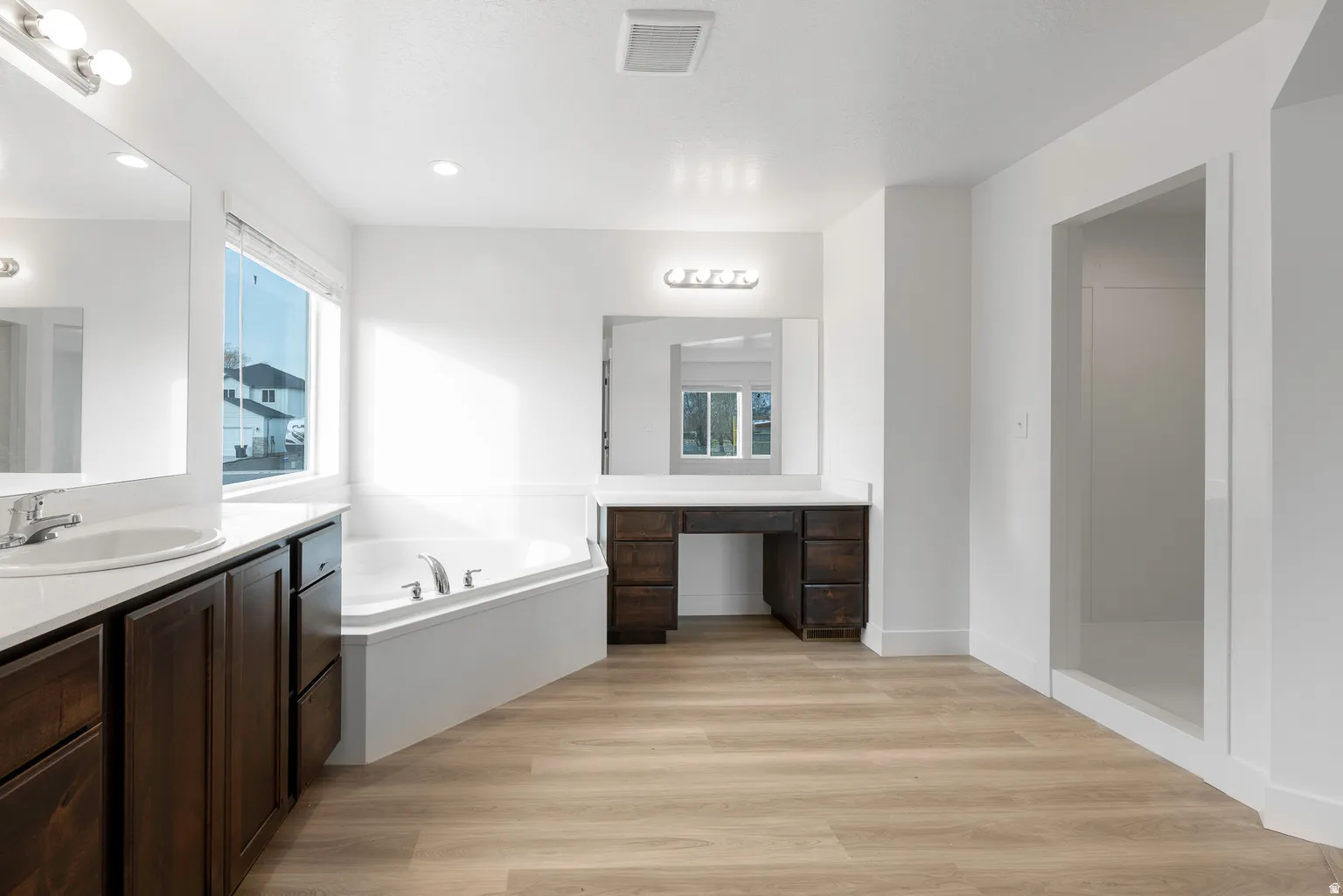 Bathroom featuring light wood-style floors, two vanities, a bath, and a walk in shower