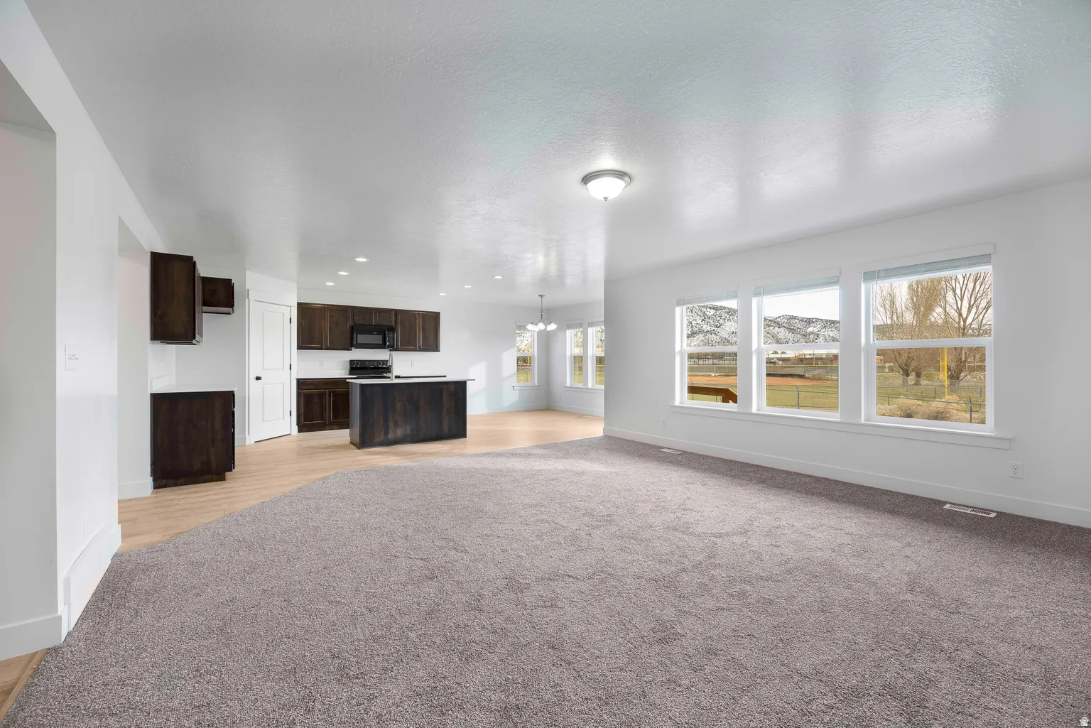 Unfurnished living room featuring suspended lighting and light colored carpet