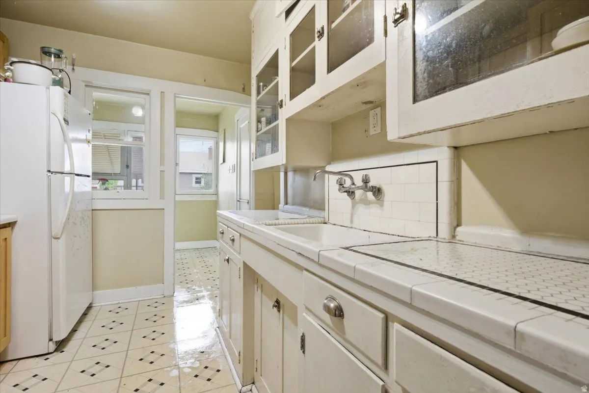 Kitchen featuring freestanding refrigerator, tile counters, white cabinets, and tasteful backsplash