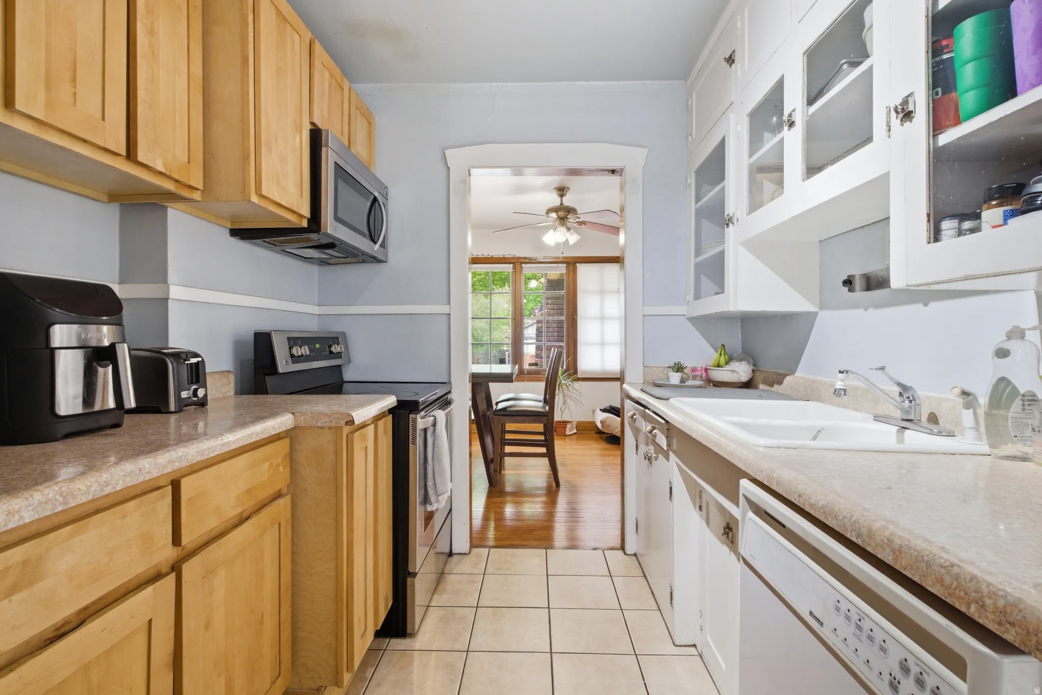 Kitchen with stainless steel appliances, light countertops, glass insert cabinets, and light tile patterned floors