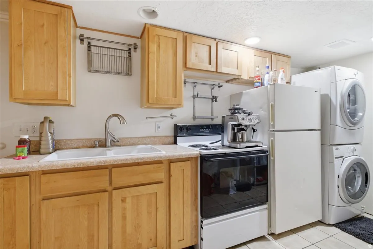 Kitchen with light wood finish cabinets, electric stove, light countertops, stacked washer and clothes dryer, and a textured ceiling
