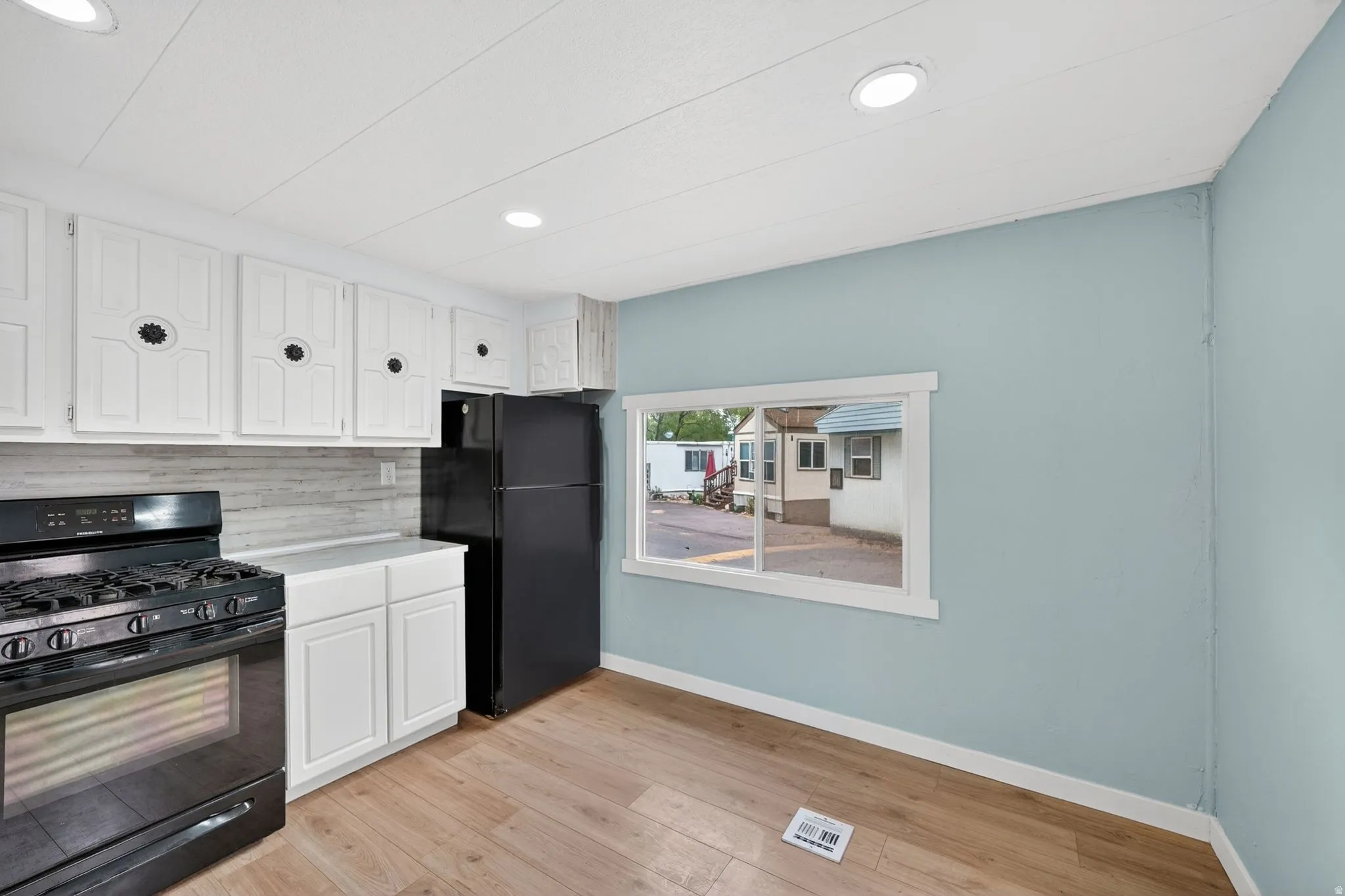 Kitchen featuring black appliances, white cabinetry, light wood finished floors, tasteful backsplash, and recessed lighting