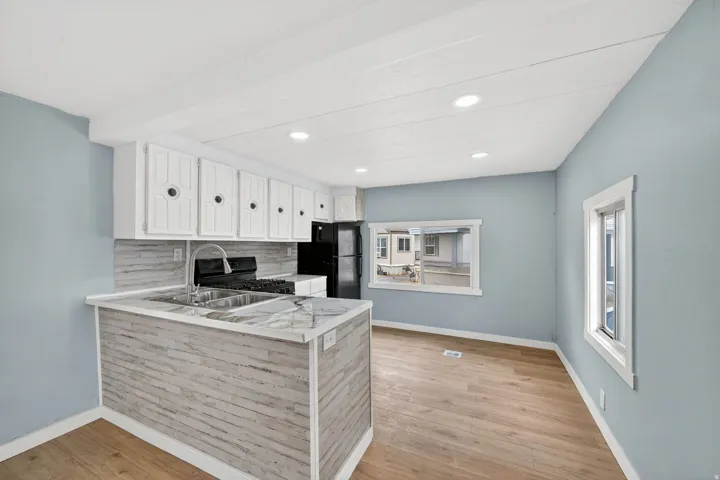 Kitchen featuring light countertops, white cabinetry, tasteful backsplash, light wood-style floors, and black appliances