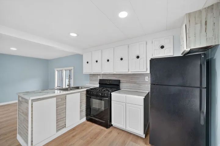 Kitchen with black appliances, a peninsula, light countertops, light wood-style flooring, and recessed lighting