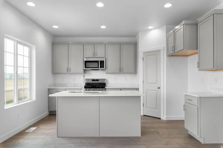 Kitchen featuring light gray cabinetry, white countertops, stainless steel appliances, and wood-finish flooring