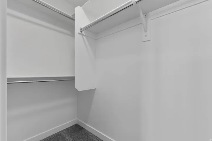 Walk-in closet featuring white walls, chrome hanging rods, an integrated shelf, and gray carpeting