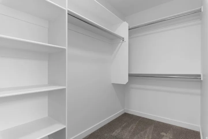 Walk-in closet featuring white built-in shelving, multiple chrome hanging rods, white baseboards, and carpet flooring