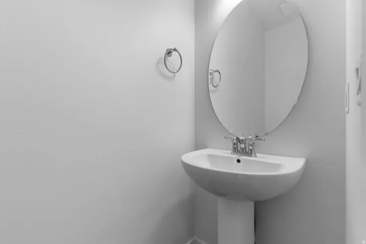Pedestal sink featuring a chrome faucet and an oval wall-mounted mirror