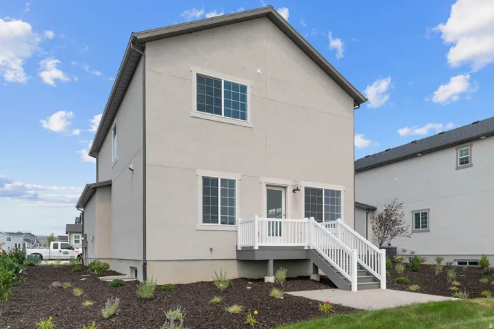 Rear exterior featuring a ground-level deck with white railing, sliding glass door, multiple windows, and a landscaped perimeter with mulch and plantings