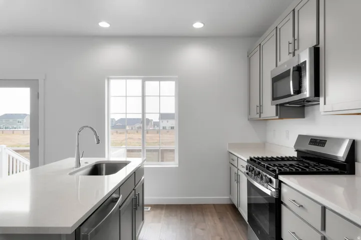Kitchen featuring a center island with undermount sink, stainless steel appliances, light-toned countertops, and wood-finish flooring