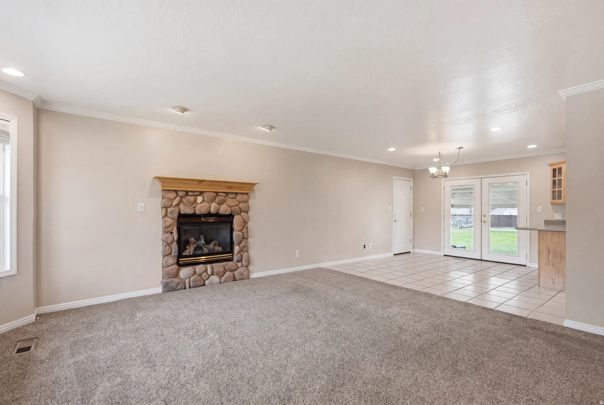 Unfurnished living room featuring light carpet, a stone fireplace, ornamental molding, french doors, and light tile patterned floors