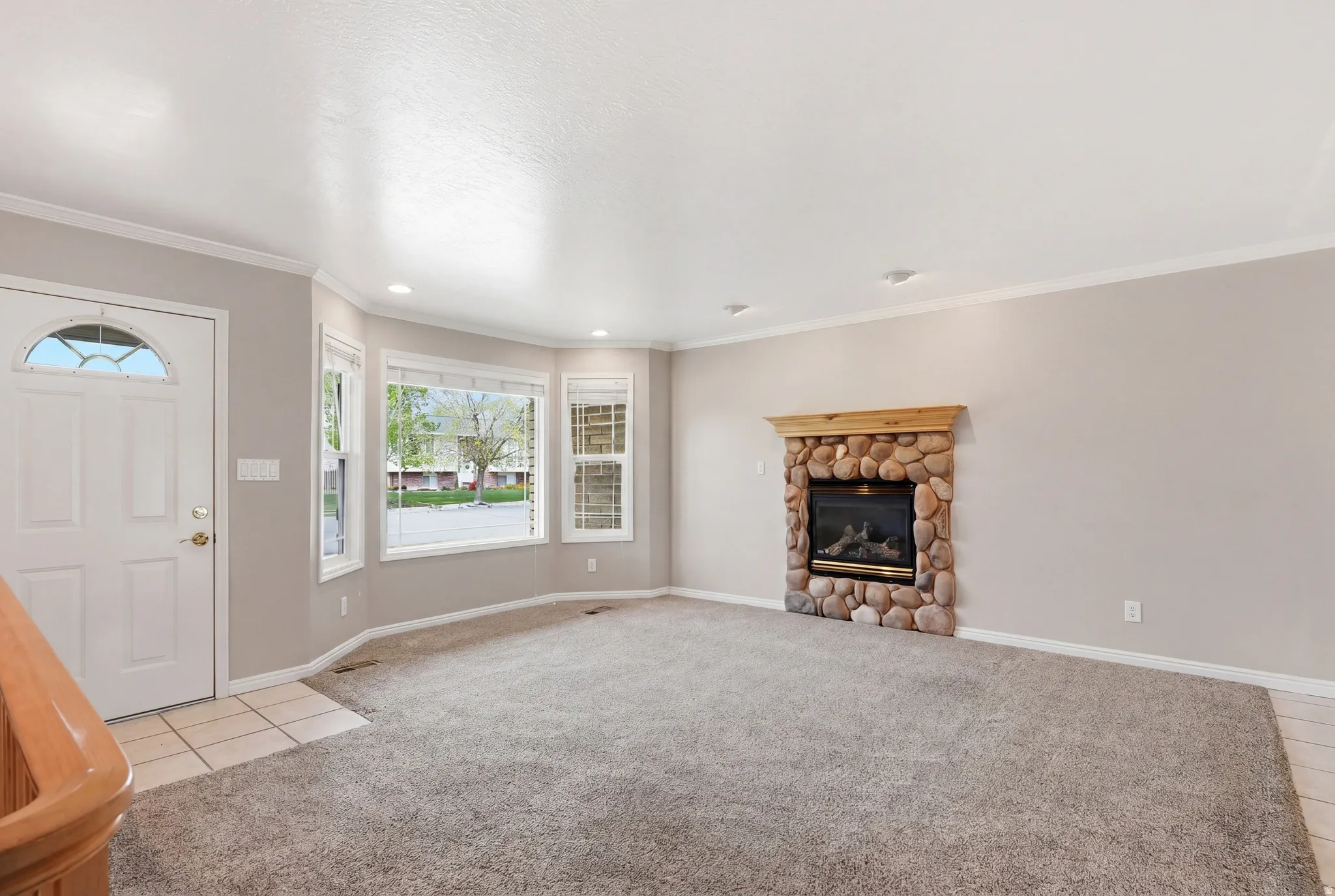 Foyer entrance featuring light colored carpet, a stone fireplace, recessed lighting, crown molding, and light tile patterned floors