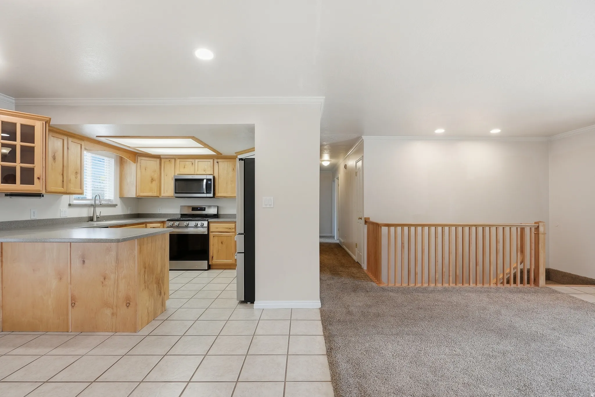 Kitchen with light carpet, glass fronted cabinets, light tile patterned floors, light wood finish cabinetry, and stainless steel appliances