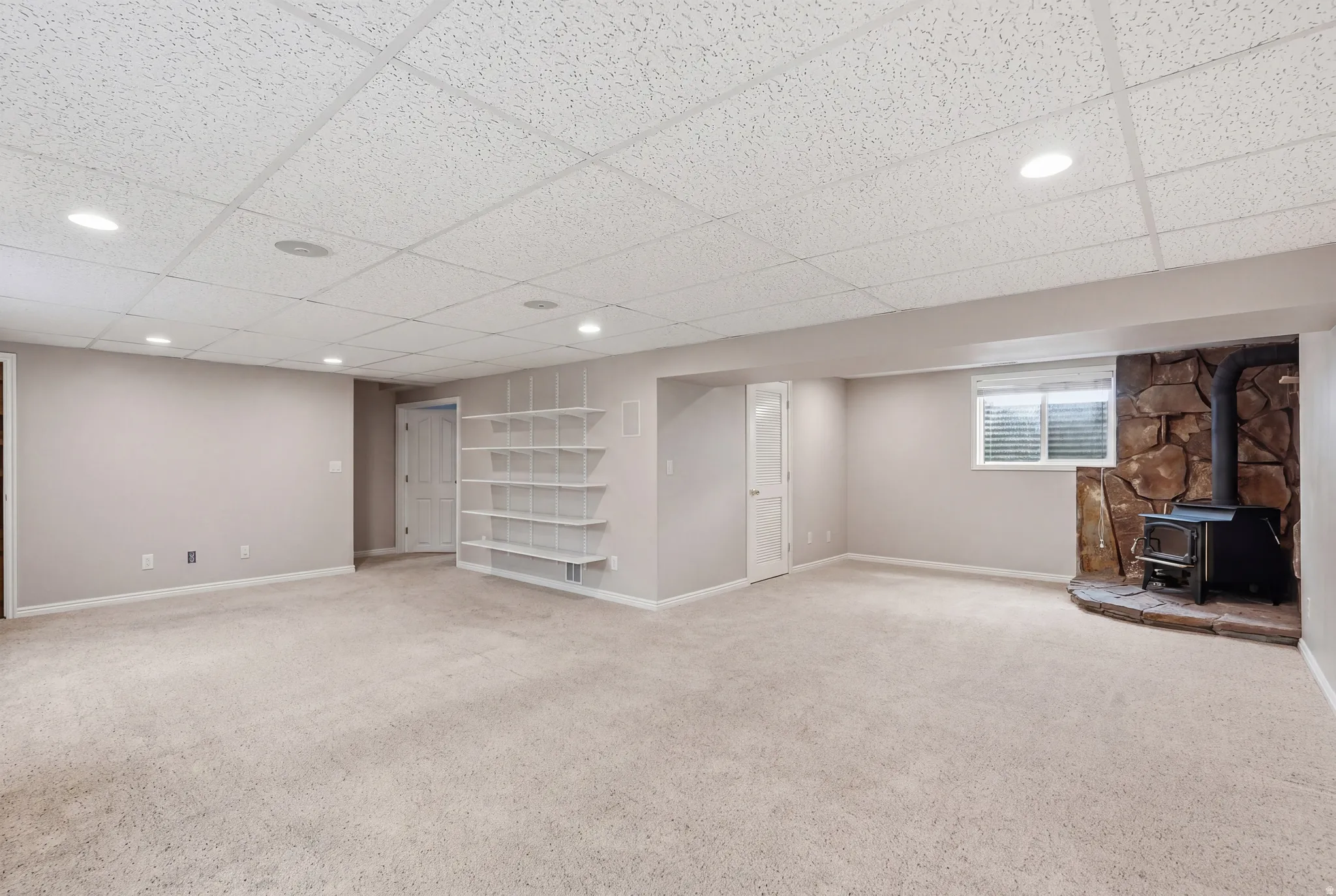 Finished basement with a wood stove, recessed lighting, a drop ceiling, and light colored carpet