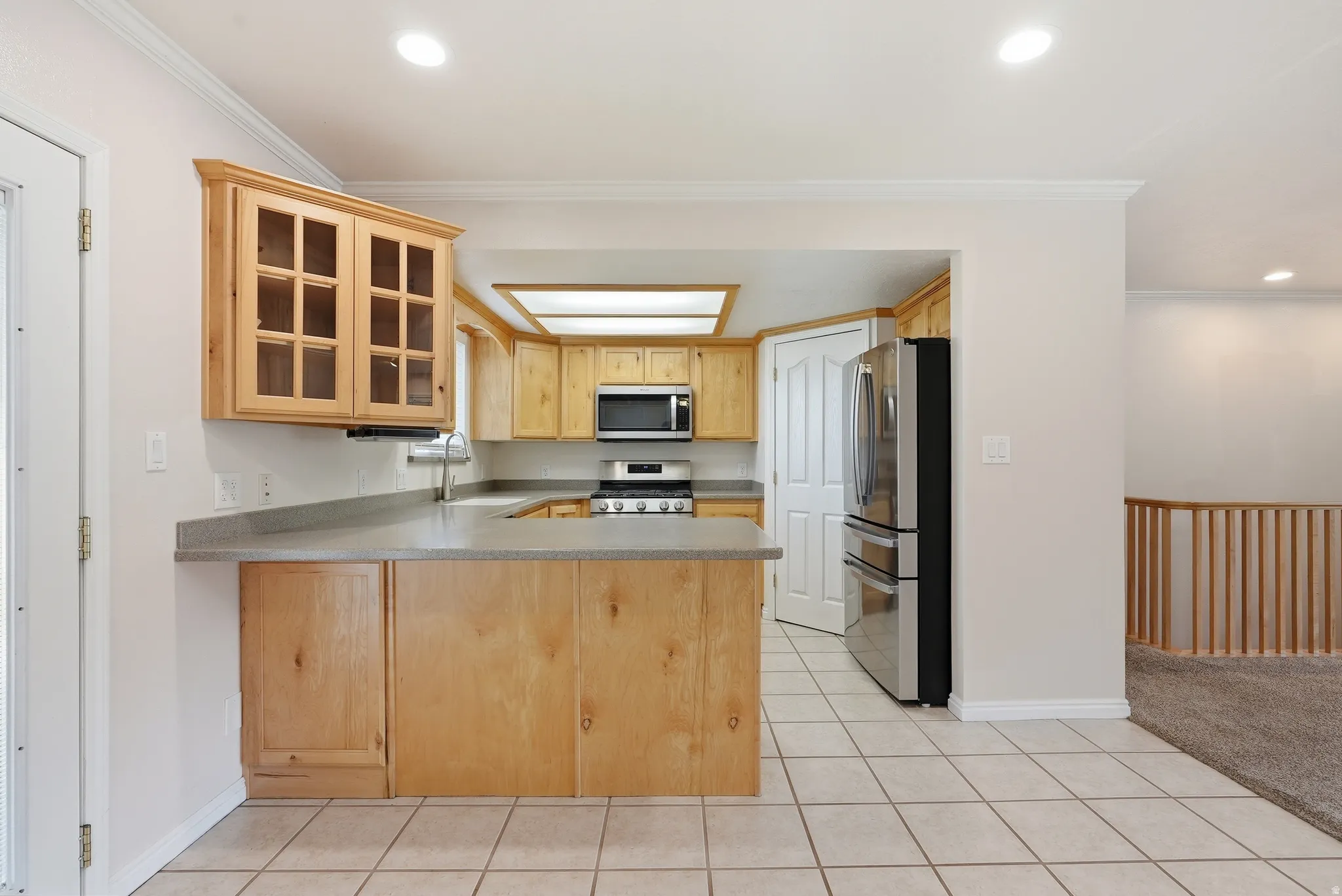 Kitchen with glass fronted cabinets, a peninsula, stainless steel appliances, recessed lighting, and light tile patterned floors