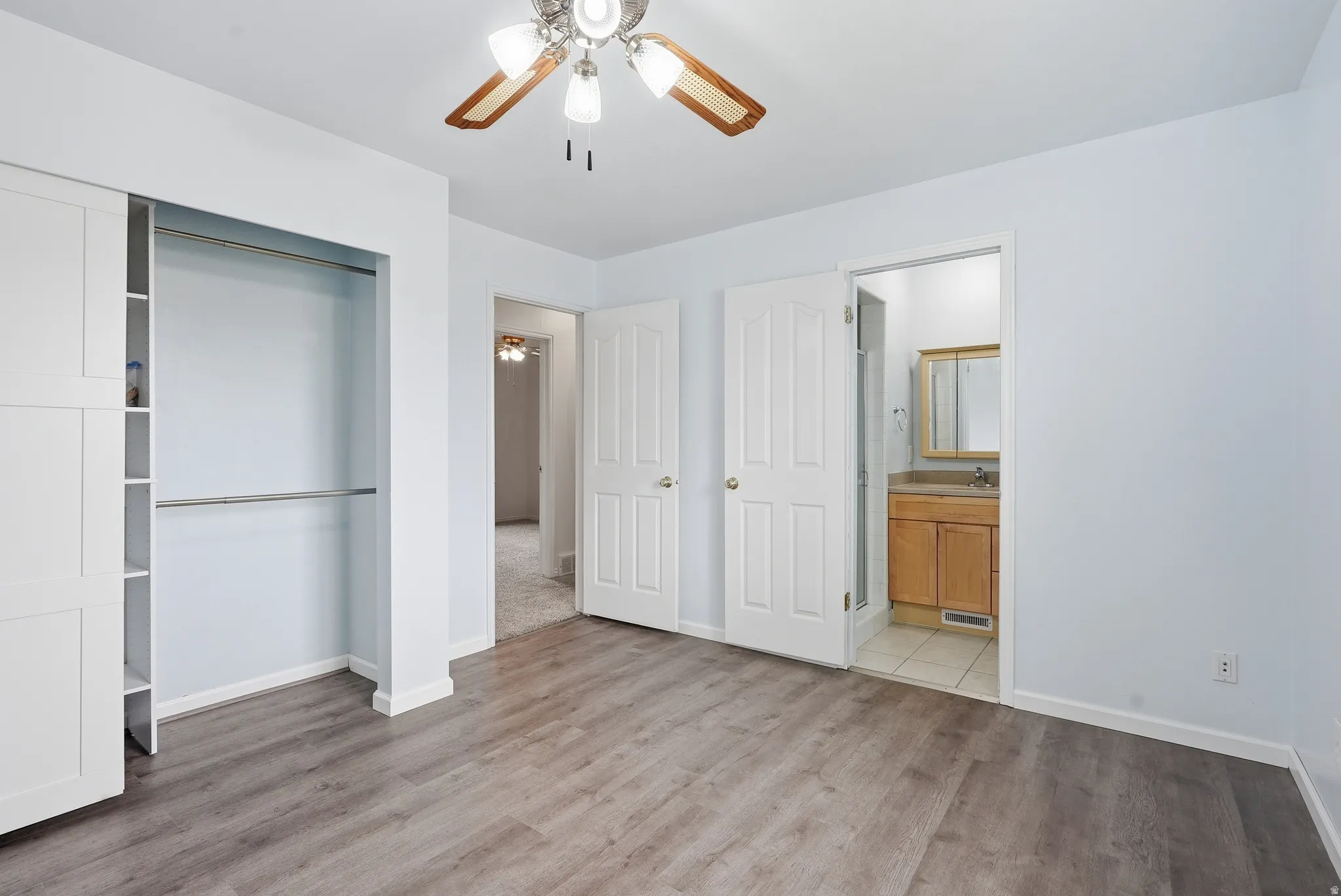 Unfurnished bedroom with light wood-style flooring, ceiling fan, connected bathroom, and a closet