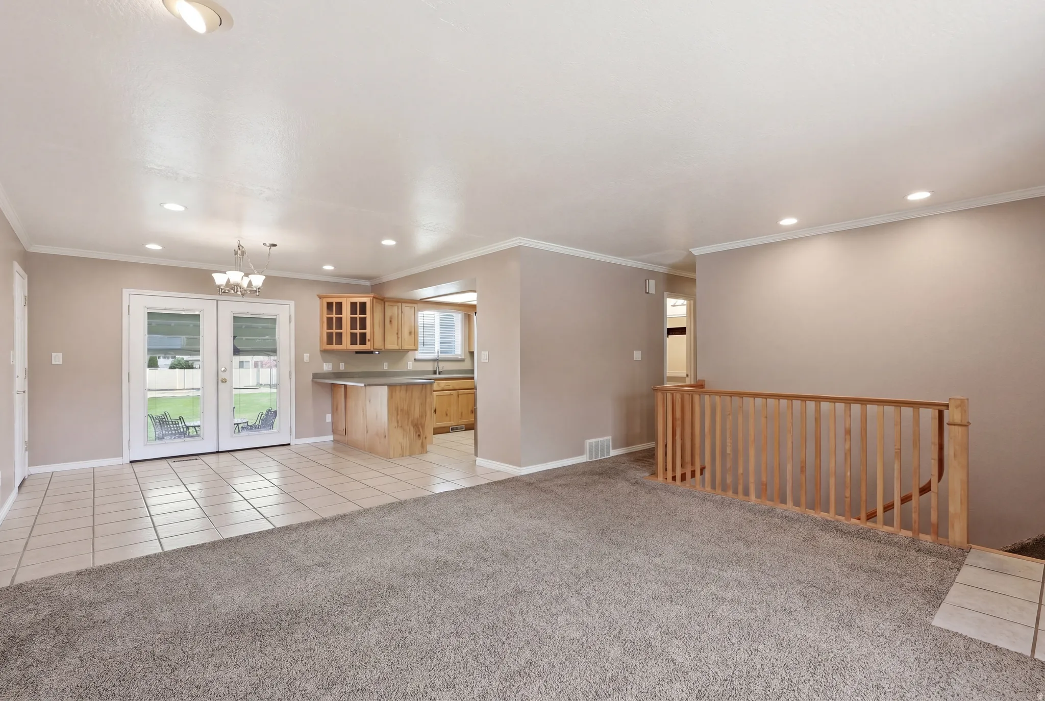 Unfurnished living room featuring a chandelier, light colored carpet, crown molding, light tile patterned floors, and french doors