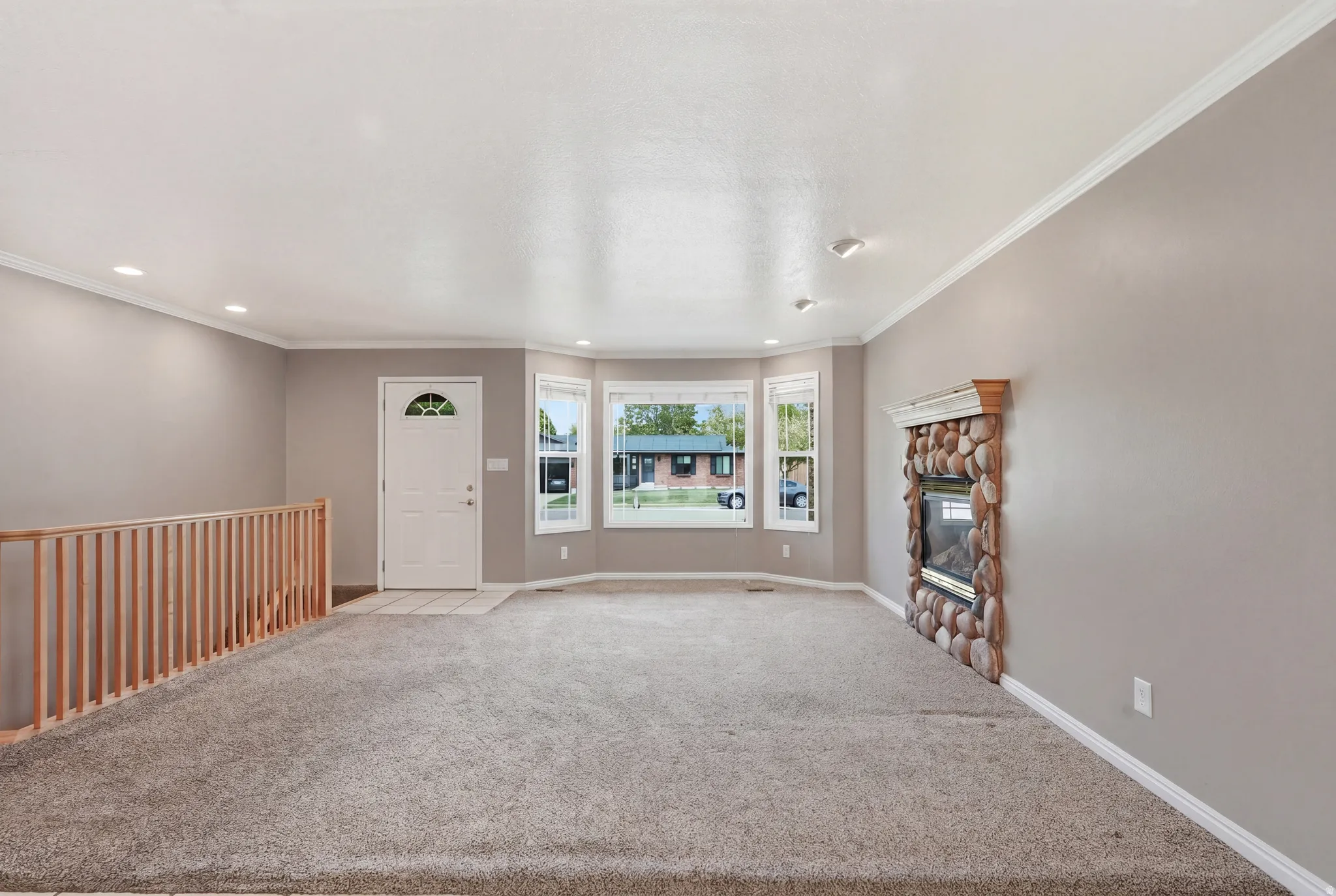 Unfurnished living room featuring carpet floors, crown molding, a stone fireplace, and recessed lighting