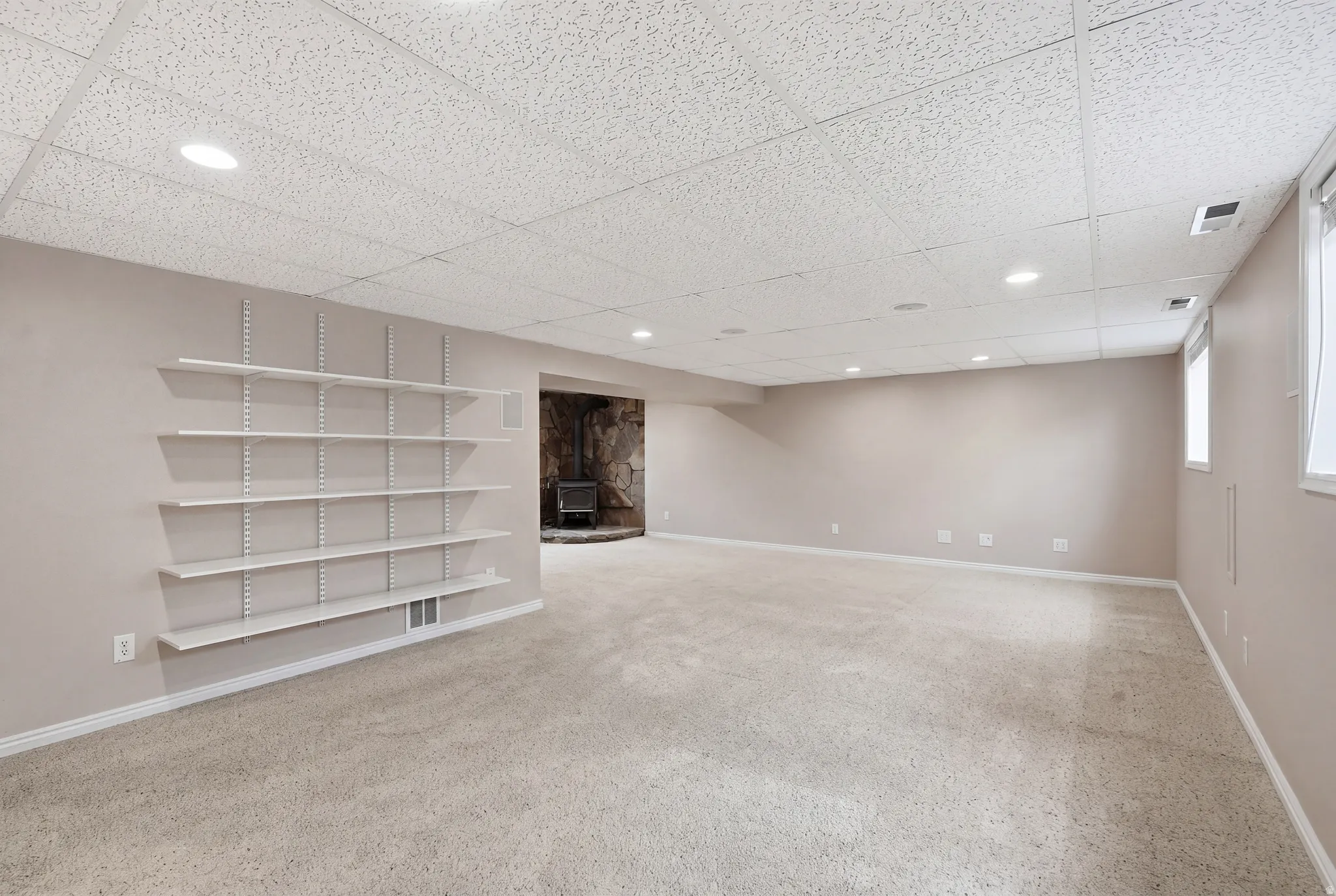 Finished below grade area with a paneled ceiling, light carpet, recessed lighting, and a wood stove