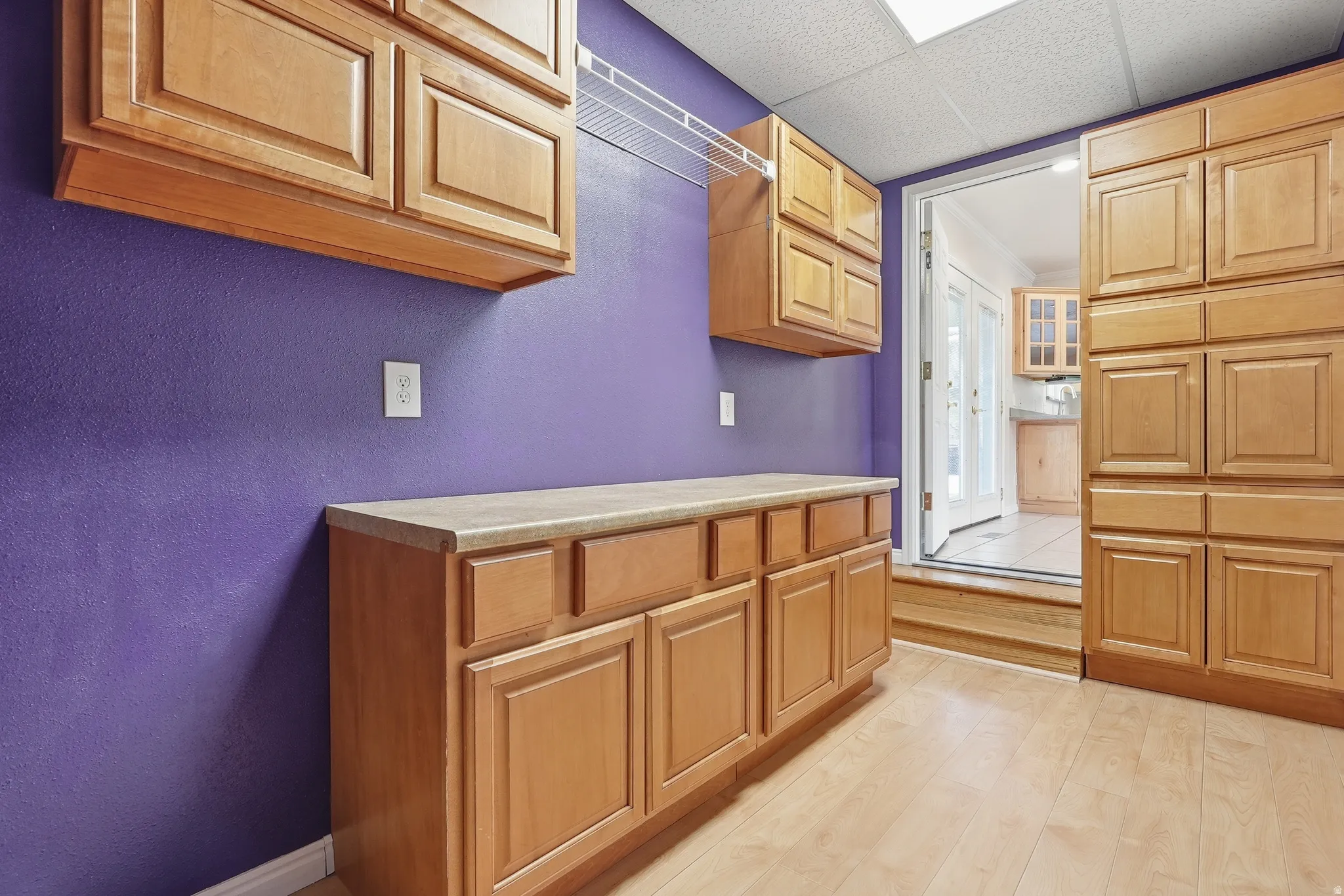 Kitchen with light wood-style floors, light countertops, a paneled ceiling, and a textured wall