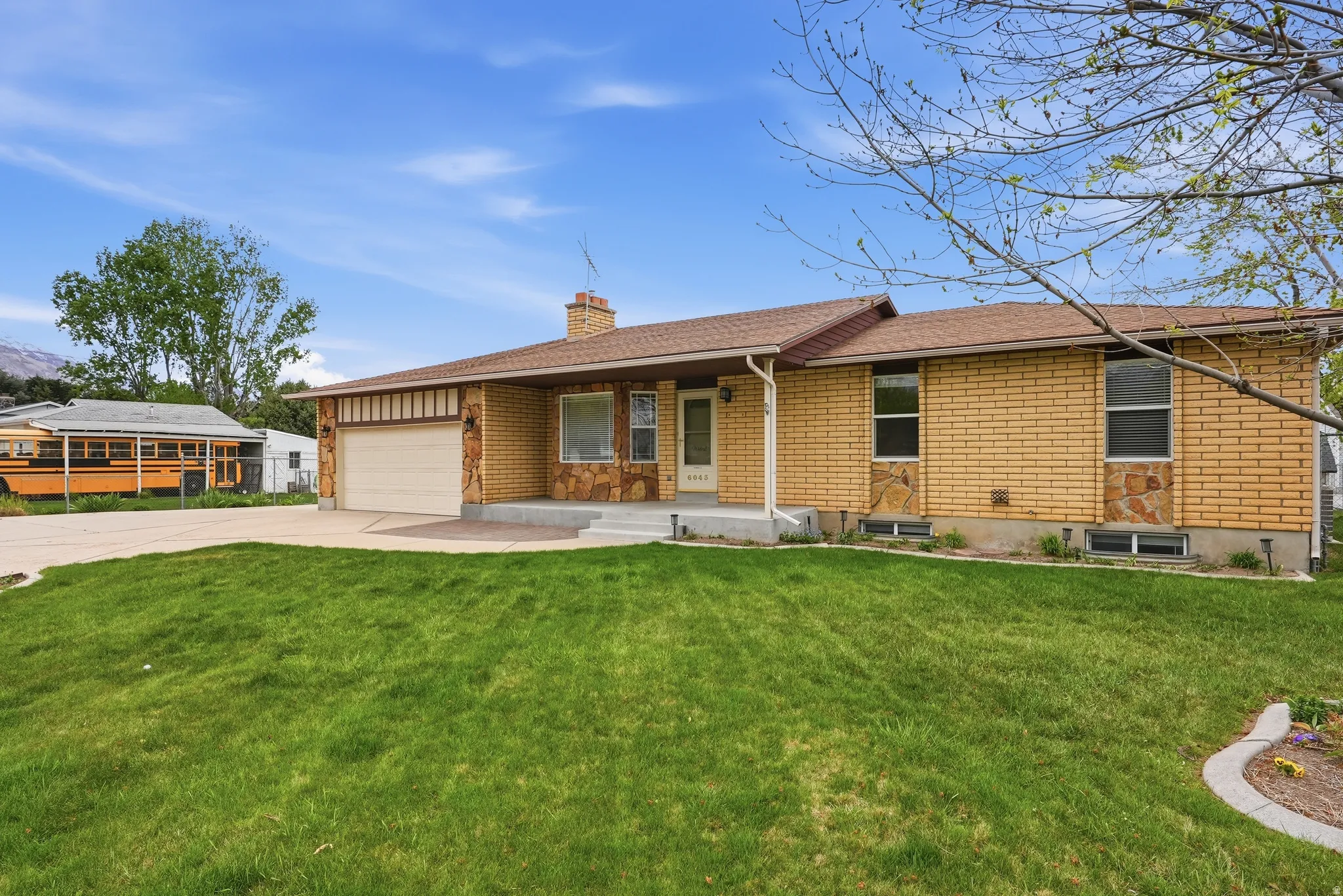 Single story home featuring brick siding, concrete driveway, covered porch, and a chimney