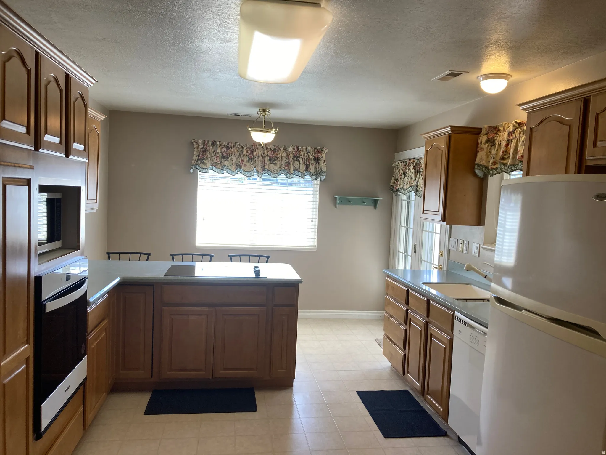 Kitchen featuring stainless steel appliances, a peninsula, wood finish cabinets, and a textured ceiling