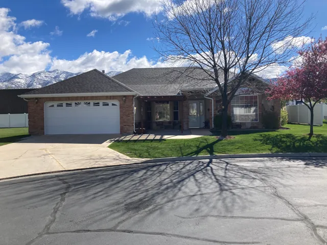 Single story home with brick siding, an attached garage, a shingled roof, concrete driveway, and a patio area