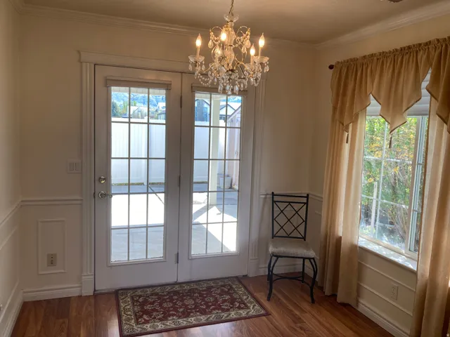 Doorway to outside with a decorative wall, wood finished floors, suspended lighting, wainscoting, and crown molding