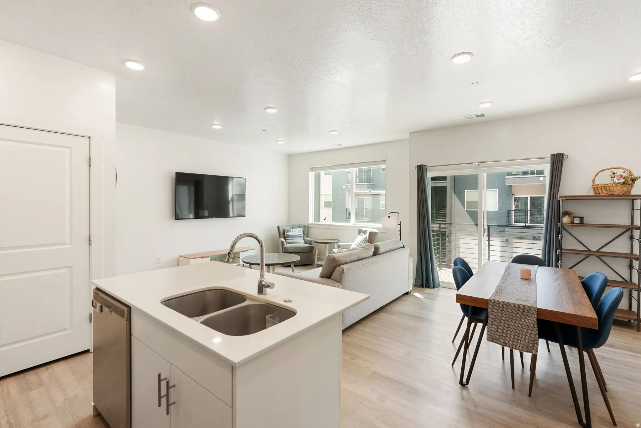 Kitchen with light wood-type flooring, a center island with sink, open floor plan, white cabinets, and stainless steel dishwasher