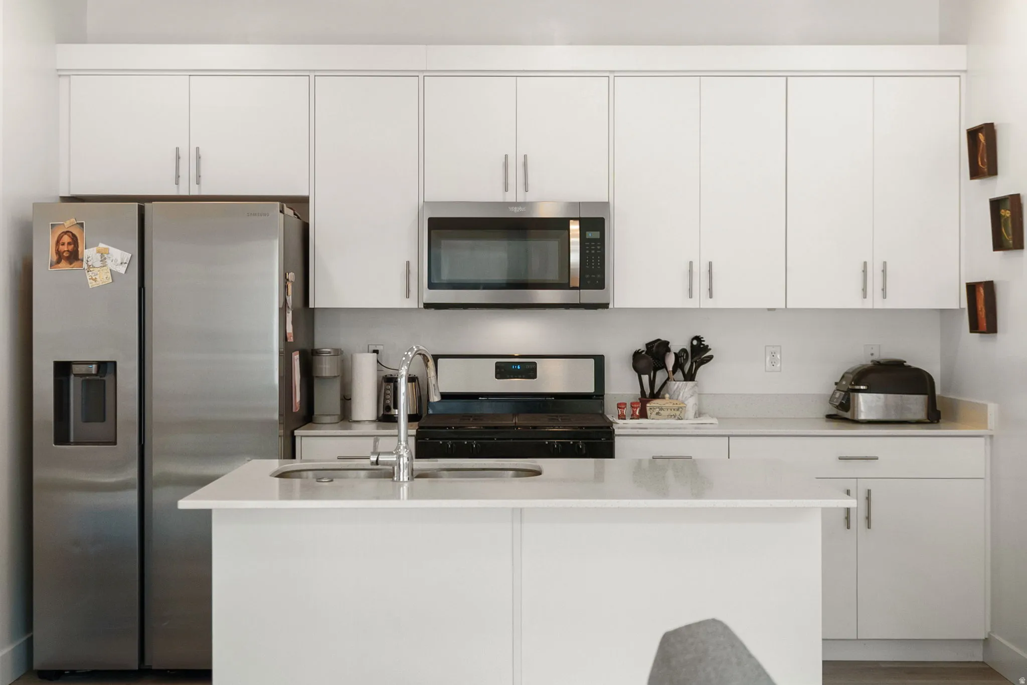 Kitchen with stainless steel appliances, a center island with sink, white cabinets, and light stone countertops