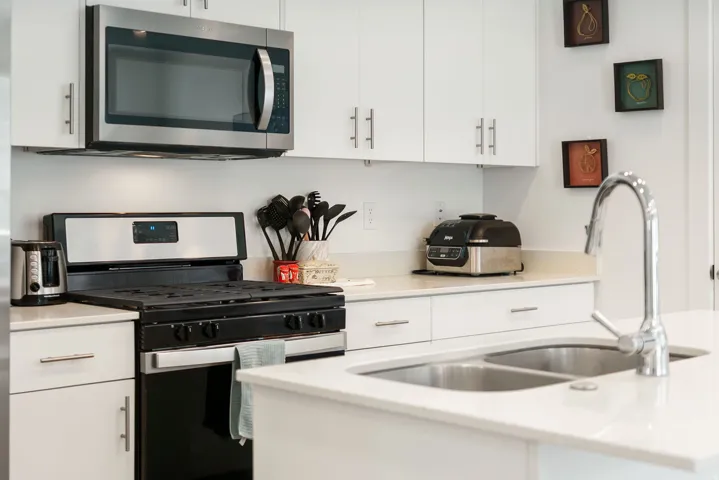 Kitchen featuring stainless steel appliances, white cabinets, and light stone countertops