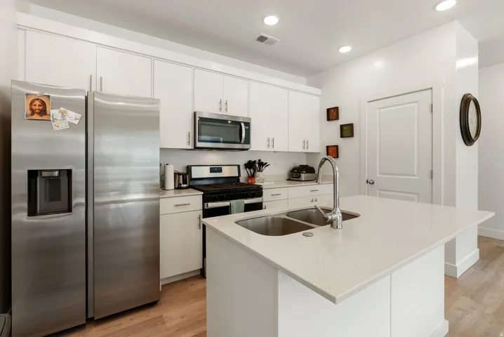 Kitchen with stainless steel appliances, light wood-type flooring, white cabinets, a center island with sink, and light stone counters