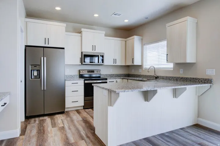 Kitchen featuring stainless steel appliances, light stone counters, a peninsula, a kitchen bar, and recessed lighting