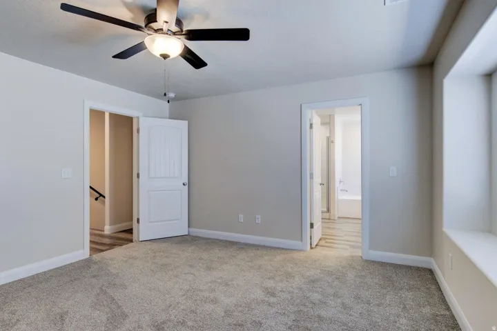 Unfurnished bedroom featuring light carpet, connected bathroom, and a ceiling fan